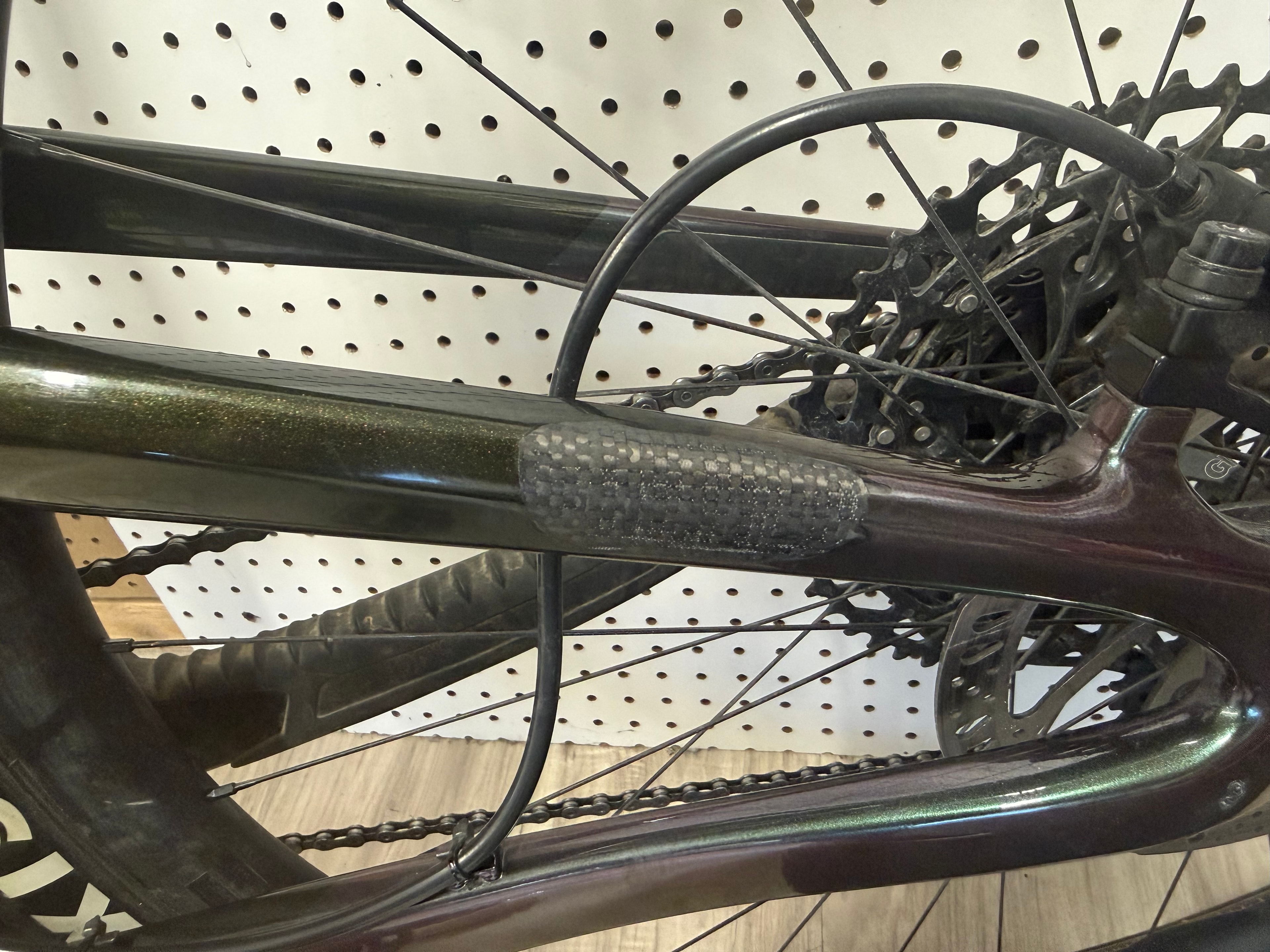 Carbon fiber seat stay repair on a dark green mountain bike frame with woven carbon patch